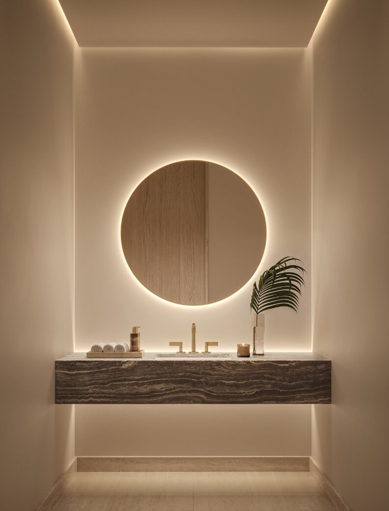 Powder room with a stone vanity and backlit circular mirror